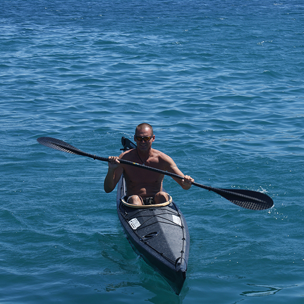 Ein Mann sitzend im schwarzen Kajak paddelt im Meer